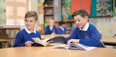 2 primary school students reading while wearing white polo shirts and royal blue sweatshirts